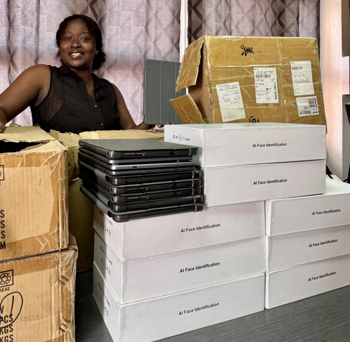 A colleague seated behind stacks of boxed tablets and AI face recognition devices