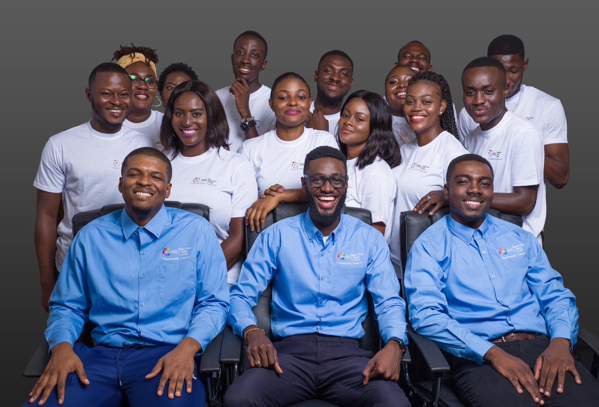 The Benny Osbon Limited team gathered in a studio, three colleagues in blue shirts seated at the front and the rest standing behind them in white tees